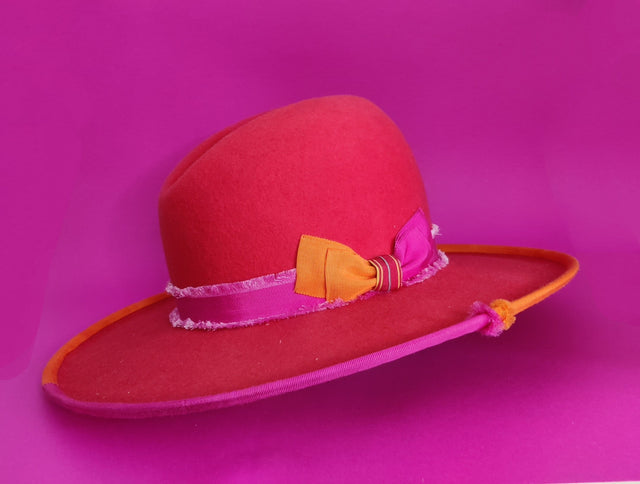 Lina Stein Red hat with a yellow band and pink bow on a purple background