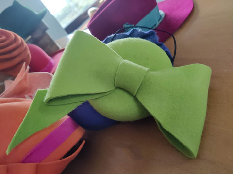 Green bow-shaped object on a wooden surface with colorful items in the background