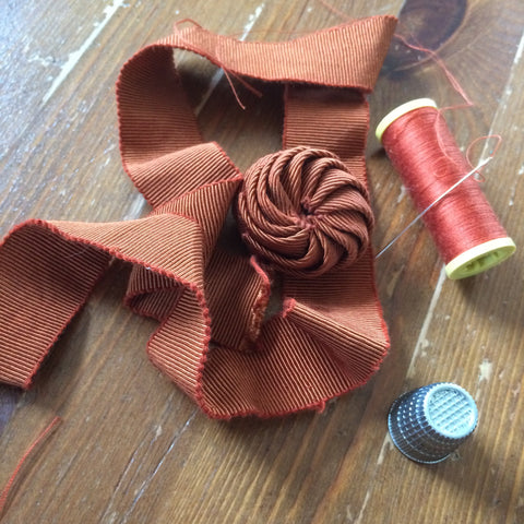 Brown ribbon with a knot on a wooden surface with spool of red thread and blue thimble.