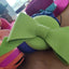 Green bow-shaped object on a wooden surface with colorful items in the background