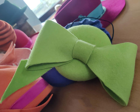 Green bow-shaped object on a wooden surface with colorful items in the background