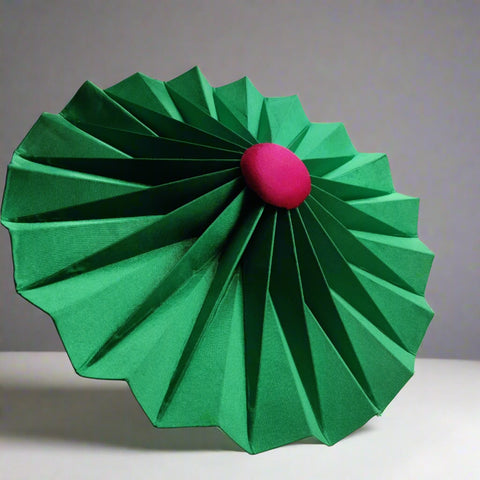 Green origami hat flower with a pink center on a white surface